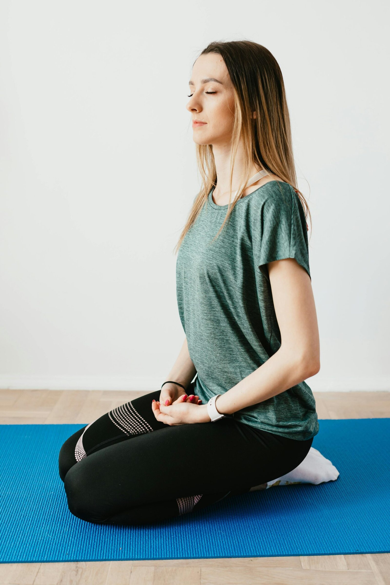 Une dame blonde est assise en tailleur sur un tapis de yoga, les yeux fermés, l'air détendu. Cela donne un aperçu de la méthodologie du coaching burn-out.